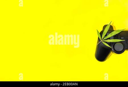 Video giochi e cannabis: Foglia di marijuana su controller di gioco nero su sfondo giallo con grande spazio di copia a sinistra. Foto Stock