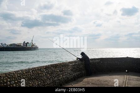 Brighton UK 11 Febbraio 2021 - UN pescatore solista affronta le temperature gelide sul lungomare di Brighton mentre le restrizioni di blocco dei governi continuano: Credit Simon Dack / Alamy Live News Foto Stock