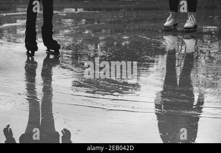 Due ragazze che pattinano sulla pista di ghiaccio che si fonde bagnato. Skater per principianti e professionisti. Concetto di raggiungimento degli obiettivi. Riflessione. Abstract vacanze invernali backgroun Foto Stock