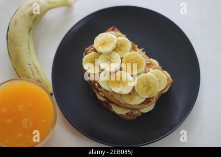 Pane tostato al miele di banana al burro di arachidi servito con succo d'arancia, un'idea facile per la colazione. Scatto su sfondo bianco. Foto Stock