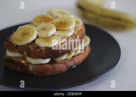 Pane tostato al miele di banana al burro di arachidi, un'idea facile per la colazione. Scatto su sfondo bianco. Foto Stock