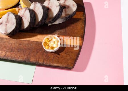 Sgombro fresco tritato giace su una tavola da cucina insieme con capsule di olio di fegato di merluzzo su uno sfondo luminoso Foto Stock