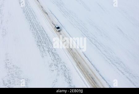 11 febbraio 2021, Schleswig-Holstein, Bornhöved: Un'automobile sta guidando su una strada completamente coperta di neve. Foto: Axel Heimken/dpa Foto Stock