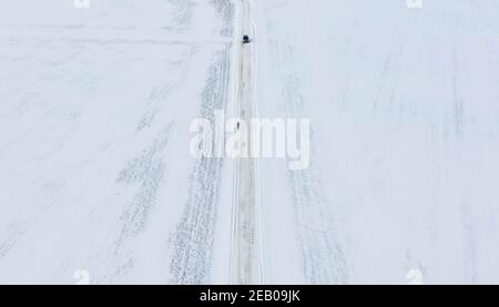 11 febbraio 2021, Schleswig-Holstein, Bornhöved: Una macchina incontra un pedone su una strada completamente coperta di neve. Foto: Axel Heimken/dpa Foto Stock