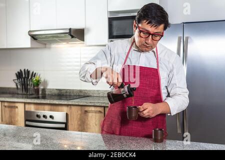 L'uomo latino serve caffè da una pressa francese a una tazza nella cucina della sua casa o in un ristorante. Foto Stock