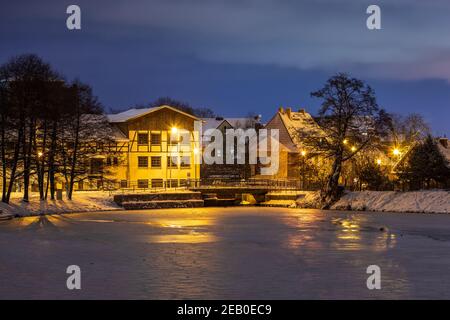 Gdansk, Oliwa, Polonia - 16 gennaio 2021 - Vista della città vecchia illuminata e innevata di Oliwa. Un vecchio mulino e un Młynski Pond congelato. Foto Stock