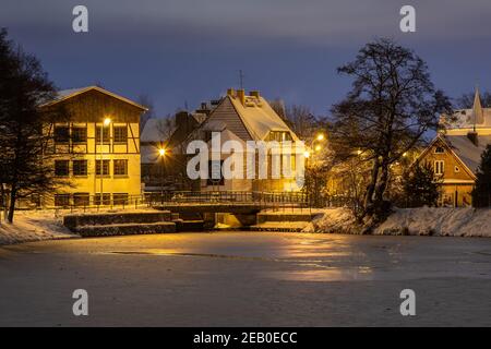 Gdansk, Oliwa, Polonia - 16 gennaio 2021 - Vista della città vecchia illuminata e innevata di Oliwa. Un vecchio mulino e un Młynski Pond congelato. Foto Stock