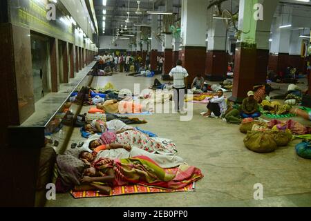 Kolkata, India - Marzo, 2014: Uomini e donne avvolti in coperte che dormono a terra nell'edificio della stazione ferroviaria di Howrah vicino ai banchi di biglietteria. Foto Stock