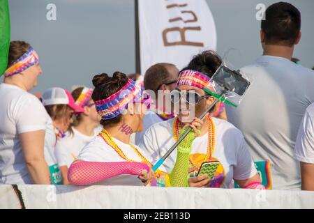 6 aprile 2019 Tulsa USA due donne che ridono e parlano in costume con telefoni e bastone selfie in attesa di inizio Di Serie colore Foto Stock