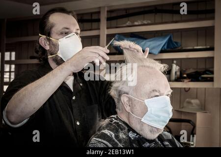 11-19-2020 - il barbiere in viaggio taglia i capelli di mans senior in garage - entrambe le maschere Foto Stock