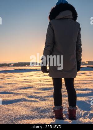 bella foto di una donna da dietro, in posa in un bellissimo campo di neve durante il tramonto Foto Stock