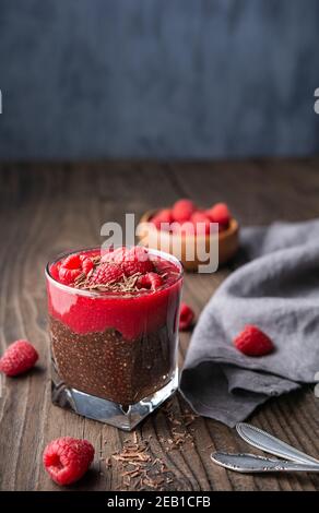 Superfood dolce vegano sano, cacao scuro pudding di semi di chia con purea di lamponi, condito con frutti di bosco freschi e trucioli di cioccolato in un vaso di vetro su Foto Stock