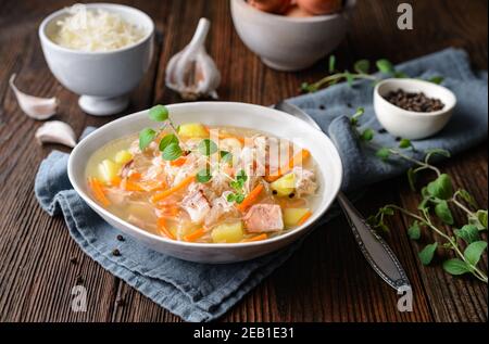 Kapusniak, zuppa polacca classica a base di crauti, costolette di maiale, pancetta affumicata, patate, carote e altre verdure in piastra di ceramica profonda su legno rustico Foto Stock