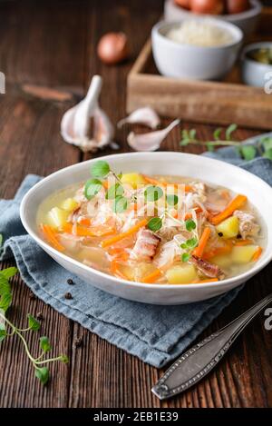 Kapusniak, zuppa polacca classica a base di crauti, costolette di maiale, pancetta affumicata, patate, carote e altre verdure in piastra di ceramica profonda su legno rustico Foto Stock