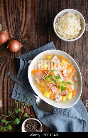 Kapusniak, zuppa polacca classica a base di crauti, costolette di maiale, pancetta affumicata, patate, carote e altre verdure in piastra di ceramica profonda su legno rustico Foto Stock
