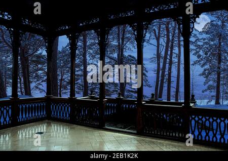 Vista dalla galleria in legno o gazebo del paesaggio invernale con pini e abeti innevati in una luna di notte stellata. Bosco di conifere Foto Stock