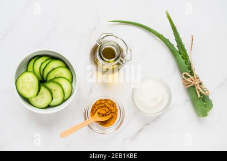 Concetto casalingo di cura della pelle. Ingredienti naturali verdi aloe vera, limone, yogurt, curcuma, cetriolo per la realizzazione di una maschera cosmetica su sfondo chiaro Foto Stock