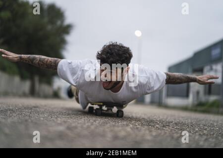 Messa a fuoco poco profonda di un bel ragazzo europeo sorridente mentendo su uno skateboard Foto Stock