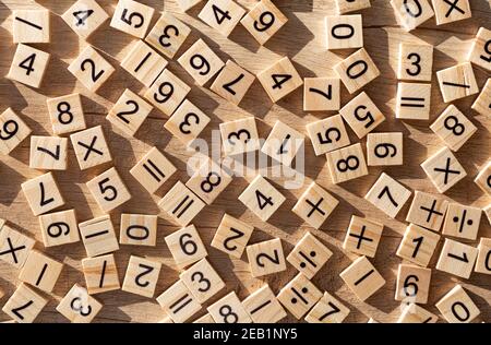 Placche di legno sparse con numeri e segni. Disposizione piatta. Materiale didattico in matematica. Foto Stock