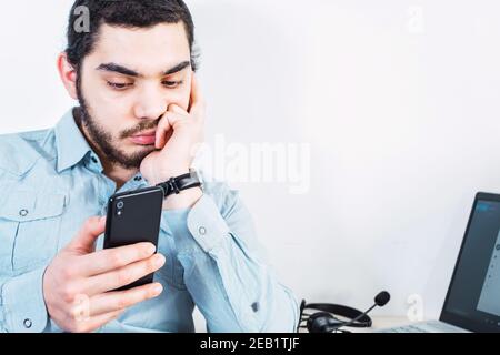 Preoccupato, giovane uomo d'affari preoccupato da casa su uno smartphone e un computer portatile Foto Stock