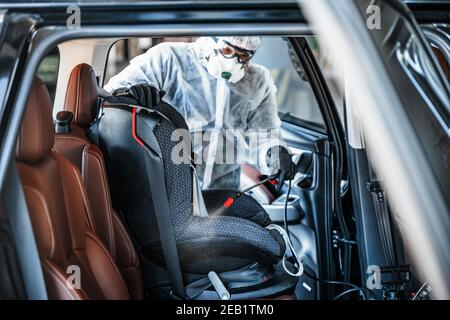 Disinfettante operaio in maschera protettiva e tuta che fa disinfezione di seggiolino per auto Foto Stock