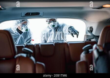 Disinfettante operaio in maschere di protezione e tute che effettua la disinfezione di sedili auto Foto Stock