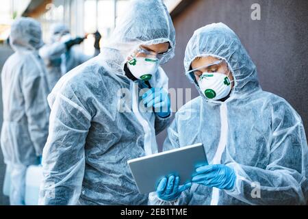 Gli operatori sanitari che indossano tute nocciole che lavorano insieme per controllare un focolaio Foto Stock