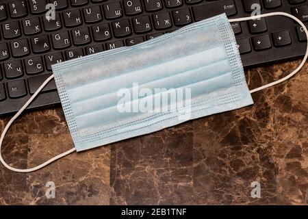 Concetto di lavoro da casa. La maschera medica protettiva si trova sulla tastiera di un computer. Quarantena durante una pandemia di coronavirus. Foto Stock