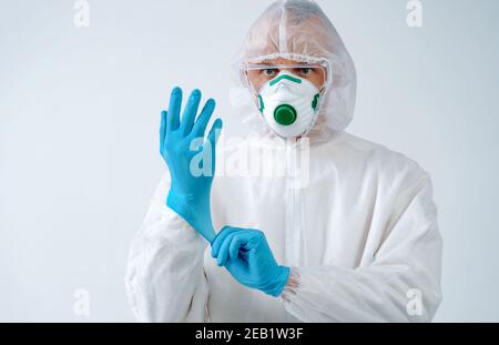 Operatore sanitario in tuta protettiva e maschera medica indossa i guanti. Concetto di assistenza sanitaria. Foto Stock