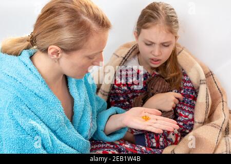 Mamma dà la sua figlia vitamine. Capsule di vitamina. Mamma e figlia. La donna tiene le vitamine in mano. Superiore, Foto Stock