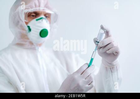 L'uomo in tuta protettiva e maschera contiene una siringa per iniezione e un vaccino. Rischio biologico. Foto Stock
