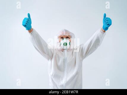 Operatore sanitario in tuta protettiva e maschera medica mostra pollici con entrambe le mani, come gesto. Foto Stock