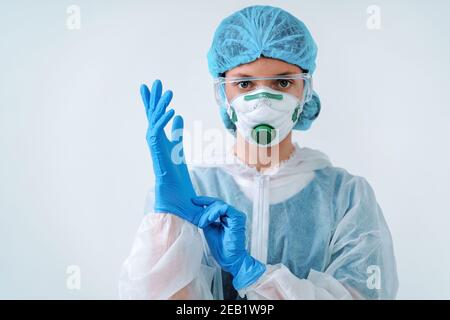 Operatore sanitario in tuta protettiva e maschera medica indossa i guanti. Concetto di assistenza sanitaria. Foto Stock