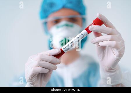 Test COVID-19 positivo. Il virologo in maschera medica e tuta protettiva contiene una provetta con campione di sangue positivo Foto Stock