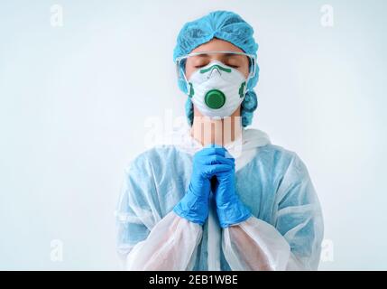 Operatore sanitario in tuta protettiva e maschera medica mettendo le mani insieme nella preghiera Foto Stock