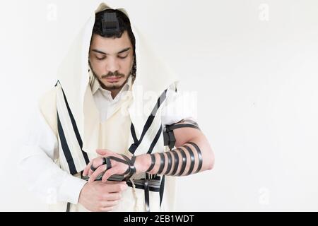 Giovane ebreo ortodosso in scialle (tallit) mettendo su filatteri (tefillin) sul braccio sinistro Foto Stock