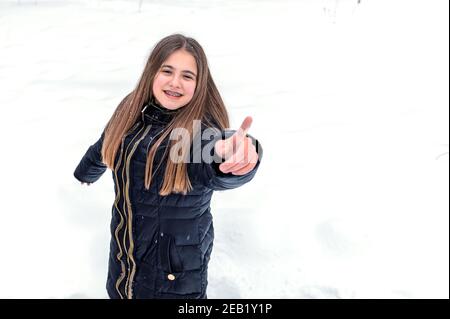 Ragazza carina sorridente e che punta alla fotocamera con un dito indice nella foresta invernale Foto Stock