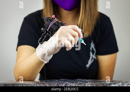 Pronto per il tatuaggio. Donna con guanto protettivo che tiene la macchina tatuatrice in studio. Occupazione creativa Foto Stock