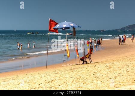 ed CALANGUTE, Goa, INDIA 3 GENNAIO 2019: Bagnino seduto nella sua sedia sotto un ombrello che guarda il mare e i turisti che vanno in acqua. D Foto Stock