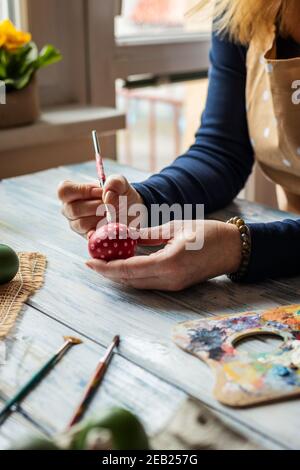 Donna che dipinge le uova di Pasqua sul tavolo a casa. Preparazione per la tradizionale celebrazione religiosa durante la settimana Santa. Decorazioni fatte in casa Foto Stock