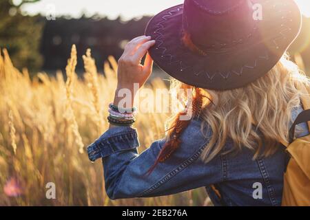 Donna bionda con cappello e giacca in denim godendo il tramonto all'aperto Foto Stock