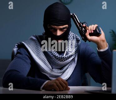 Il terrorista ladro con la pistola lavorando al computer Foto Stock