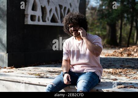 Ritratto di bel giovane Afro uomo che parla sul cellulare Telefono e seduta fuori durante l'autunno Foto Stock