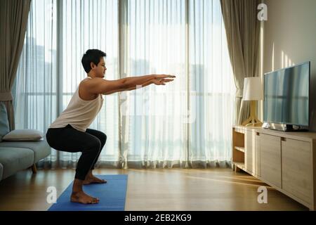 Gli uomini asiatici si esercitano a casa da squat in palestra chiusure durante COVID-19 focolaio. Foto Stock