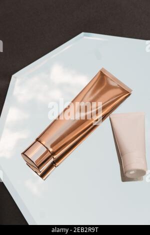 Due di tubi cosmetici bianchi e dorati su fondo specchio, prodotto di bellezza, pacchetto di branding mockup, minimalista, vista dall'alto Foto Stock
