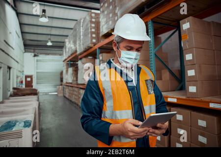 Ritratto di un operaio maschile che indossa una maschera protettiva in fabbrica warehouse con tablet digitale Foto Stock