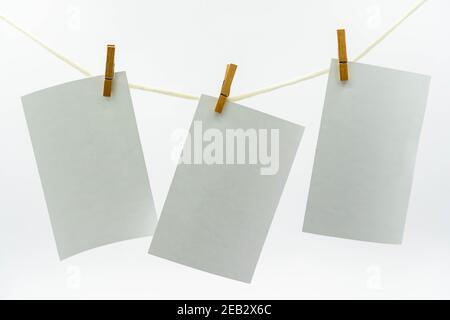 Fogli di carta vuoti multipli per le note che pendono su una corda con le stope e isolati su bianco. Foto bianca vuota appesa al concetto di corda Foto Stock