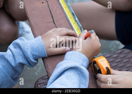 Il bambino sta riparando legno con una matita e nastro misura Foto Stock