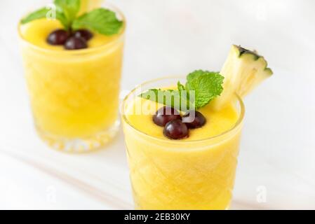 Bevande rinfrescanti sane frullato di frutta di ananas guarnite con le bacche sopra piano di appoggio in marmo bianco Foto Stock