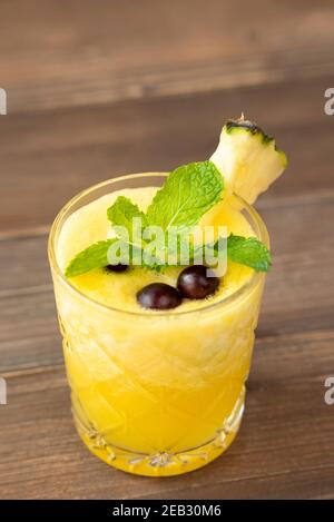 Rinfrescante sano frullato di frutta di ananas bevanda guarnita con bacche sopra tavolo in legno Foto Stock